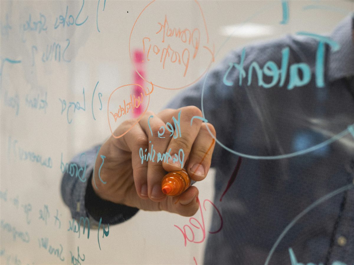 Person writing a strategy diagram on a glass board